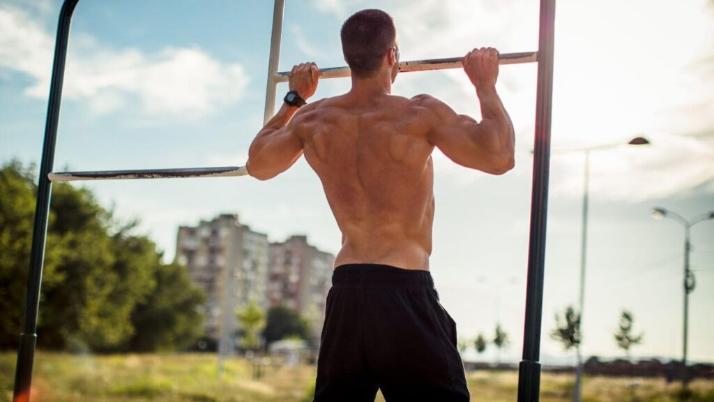 man performing a negative pull-up outside in the park.