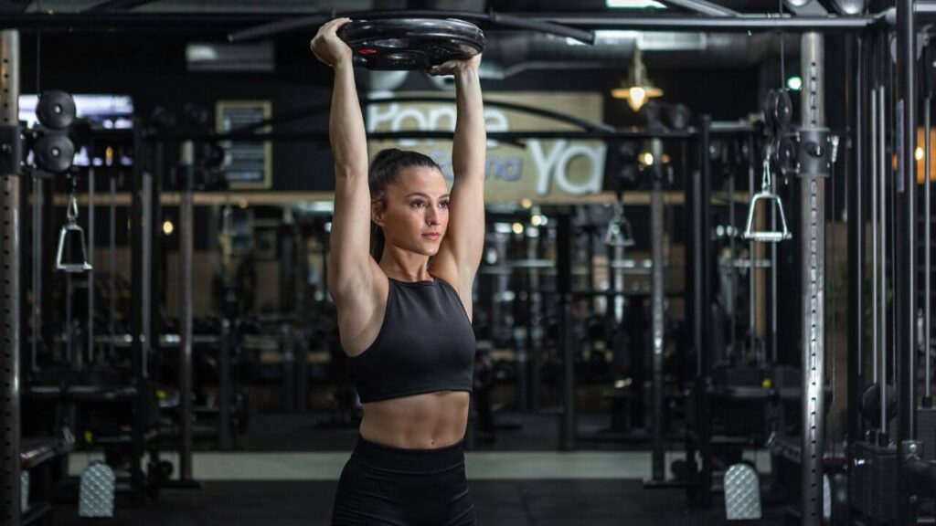 woman does overhead press with a weight plate in the commercial gym