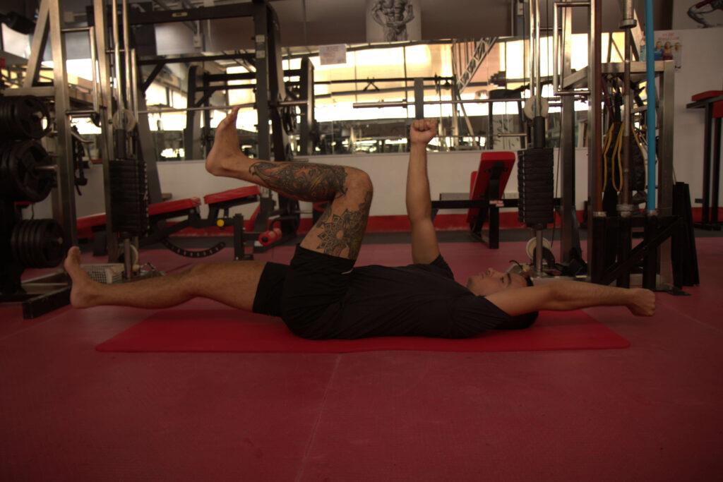 Man performs dead bug core exercise lying on his back in the gym.