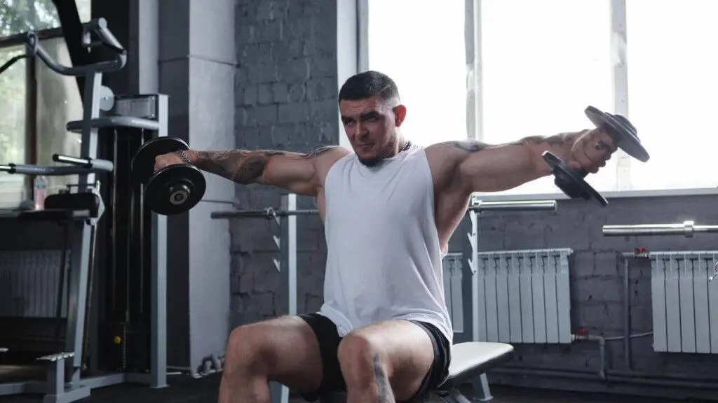 Man doing dumbbell side lateral raises during hypertrophy training.