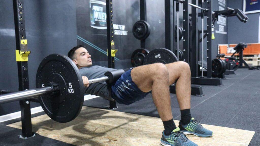Radomir performs hip-thrust exercise with the loaded barbell.