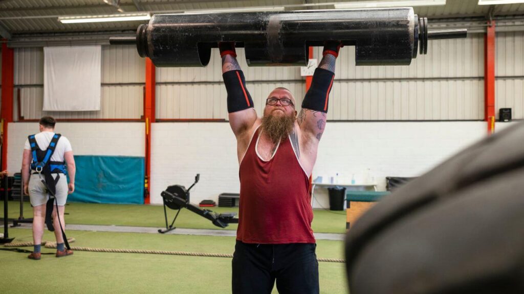 Strongman performs a log barbell overhead press