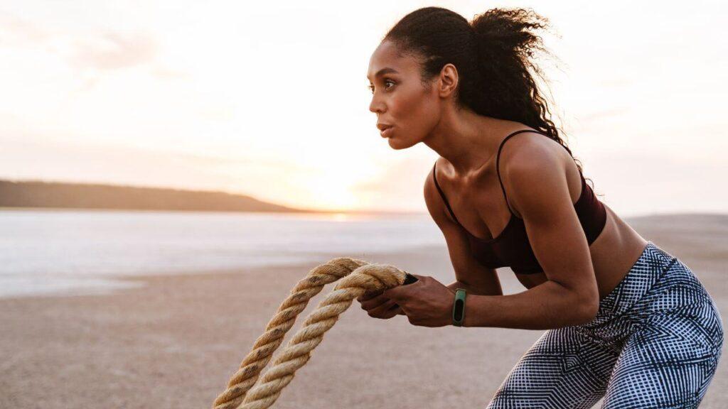 A woman works out with battle ropes outside on the beach.