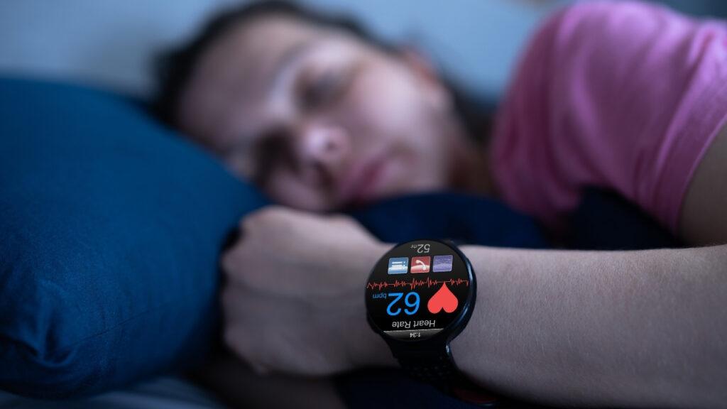The image shows a woman sleeping in bed and the fitness tracker that performs sleep tracking.