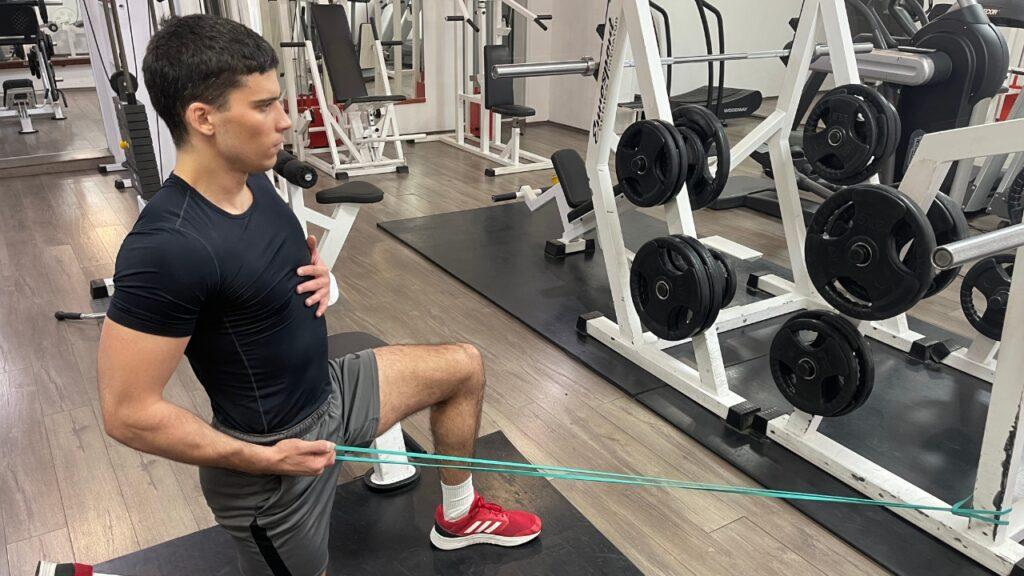 Vanja performs a single-arm, lat-row resistance band alternative exercise in the half-kneeling position.